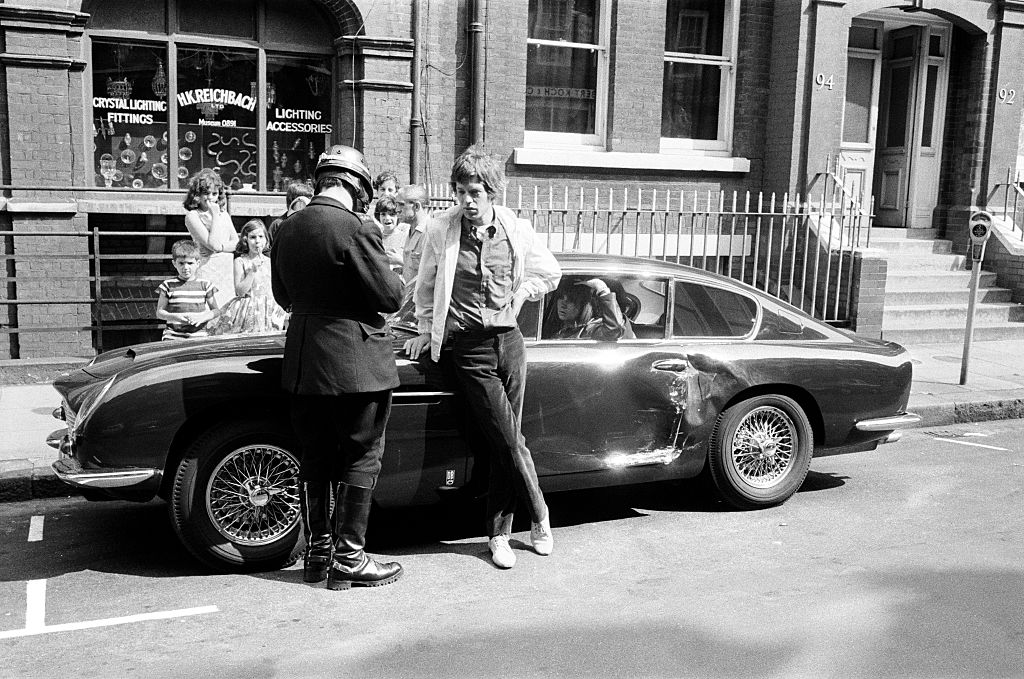 Mick Jagger has his particulars taken by a patrolman after his midnight blue Aston Martin DB6 was involved in collision with a Kraft Foods van, August 28 1966