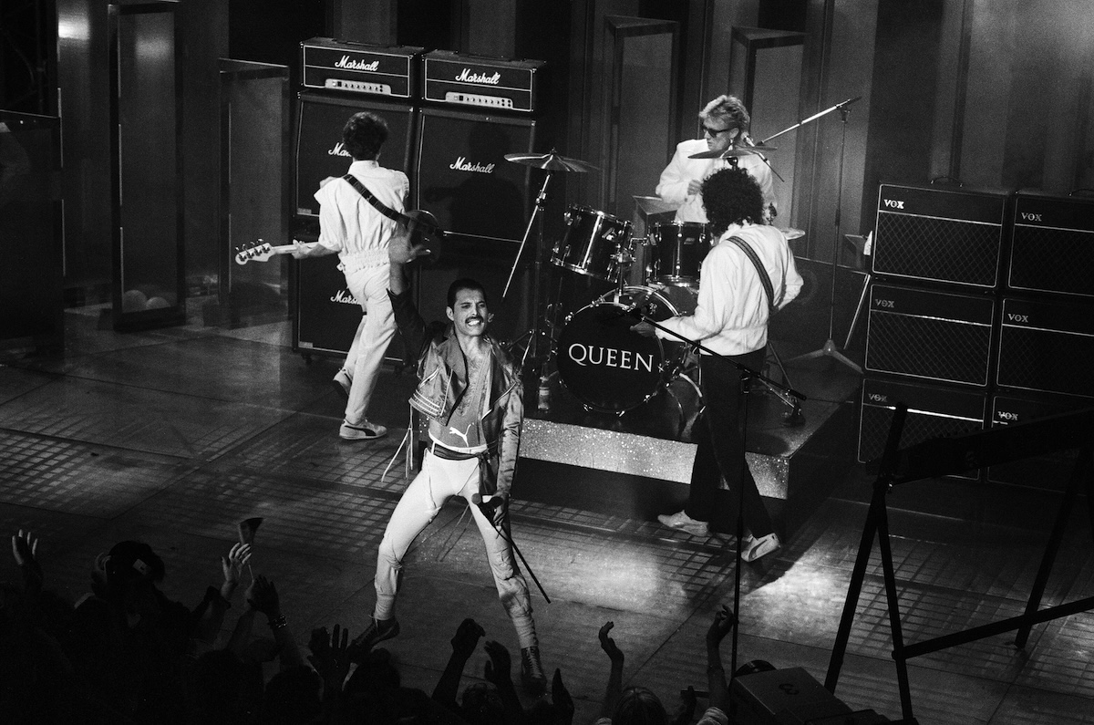 Black and white photo of Queen perform at the Golden Rose Pop festival in Montreux, Switzerland. Pictured is lead singer Freddie Mercury leading the band on stage.