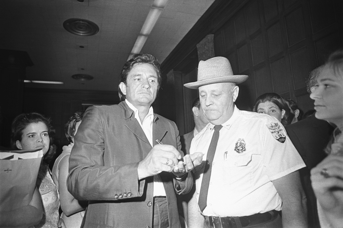 Johnny Cash (L) signs autographs outside the Governor's office after arriving in this city to do a show for prisoners connected with the early release program. At right is Walker County Sheriff Ralph Jones, who in 1967 inspired Cash to 