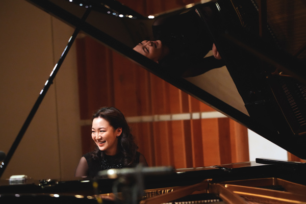 Young woman sat at an open grand piano smiling