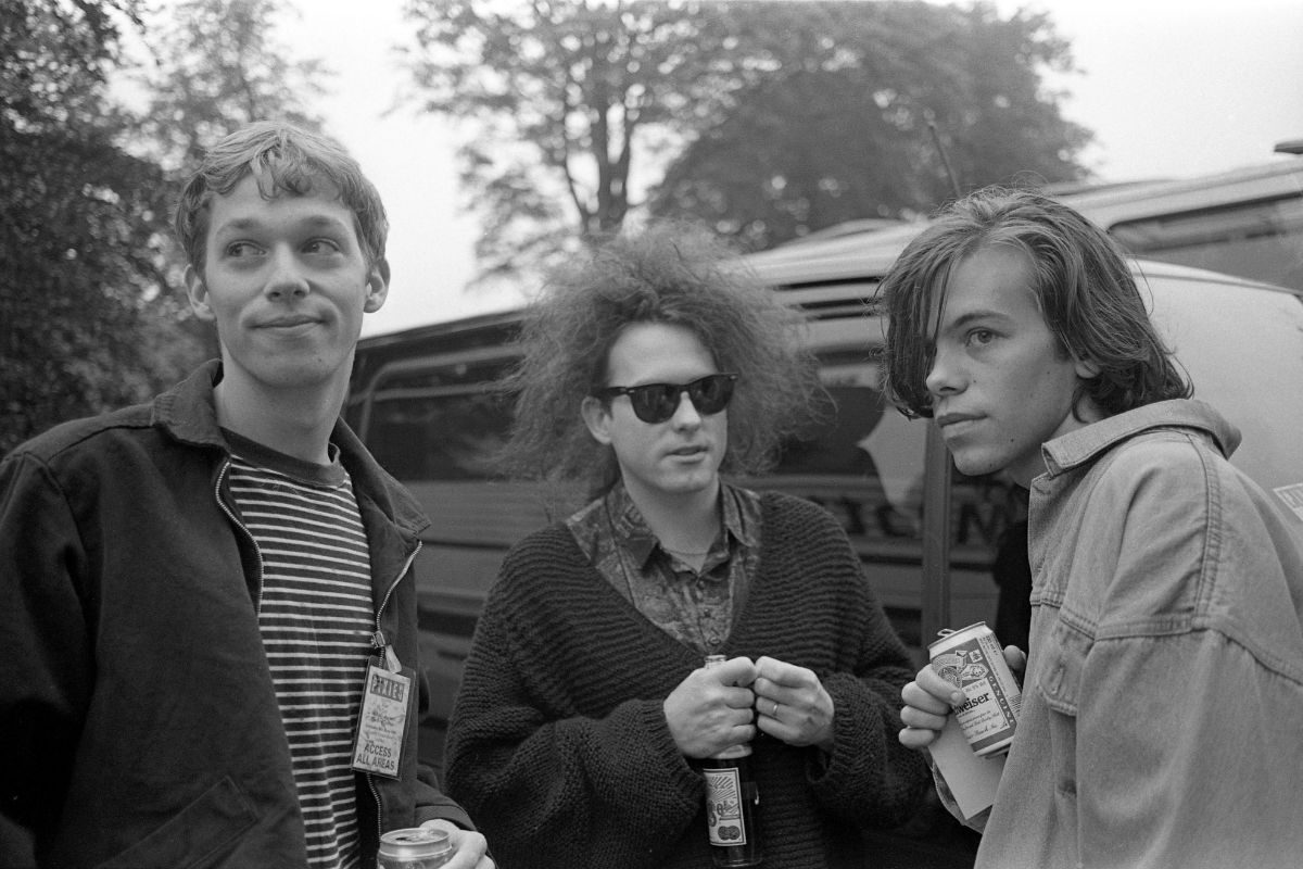 Andy Bell (left) and Mark Gardener (right) of Ride talk to Robert Smith of The Cure (centre) backstage at Crystal Palace Bowl before a concert by The Pixies, London, United Kingdom, 8th June 1991