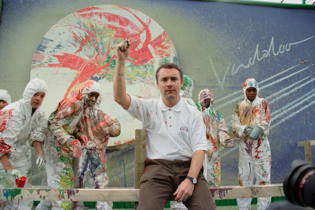 Damien Hirst sits in front of a painted billboard for a promotional event to launch the debut single 'Vindaloo' by the British band Fat Les, London, 1998