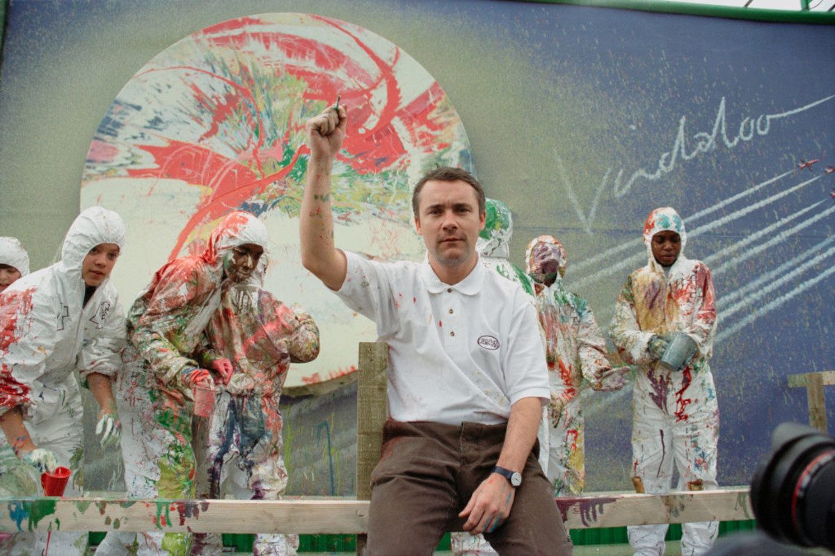 Damien Hirst sits in front of a painted billboard for a promotional event to launch the debut single 'Vindaloo' by the British band Fat Les, London, 1998