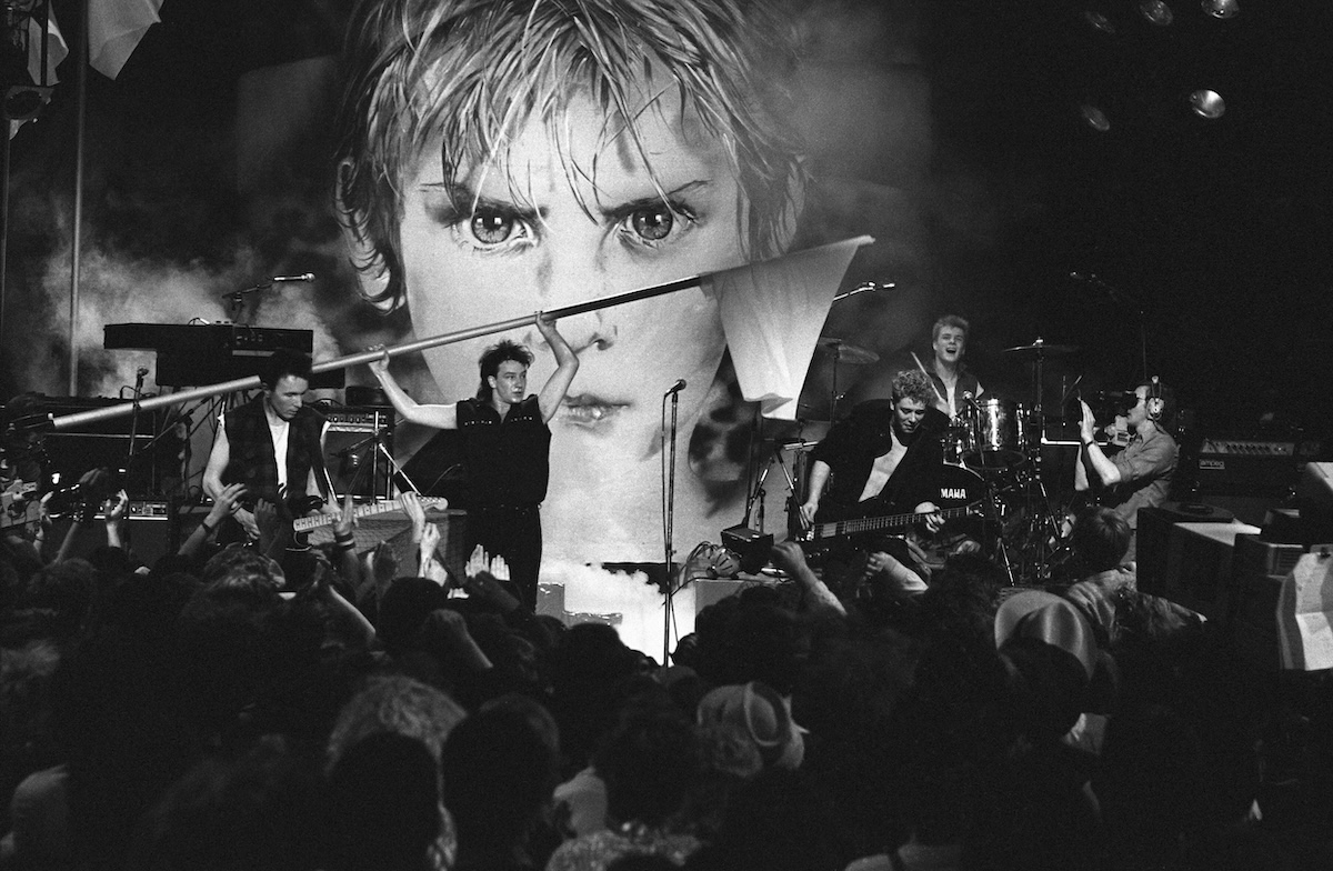 Black and white Photo of U2; L-R: The Edge, Bono (waving flag), Adam Clayton, Larry Mullen Jnr performing live on The Tube TV Show