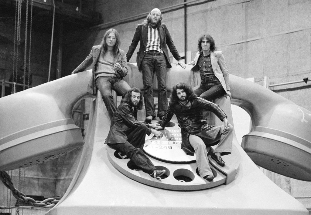 British progressive rock band Gentle Giant posing on a giant model of a telephone, UK, 1974. Clockwise, from top, centre: drummer John Weathers, bassist Ray Shulman, singer Derek Shulman, keyboard player Kerry Minnear and guitarist Gary Green
