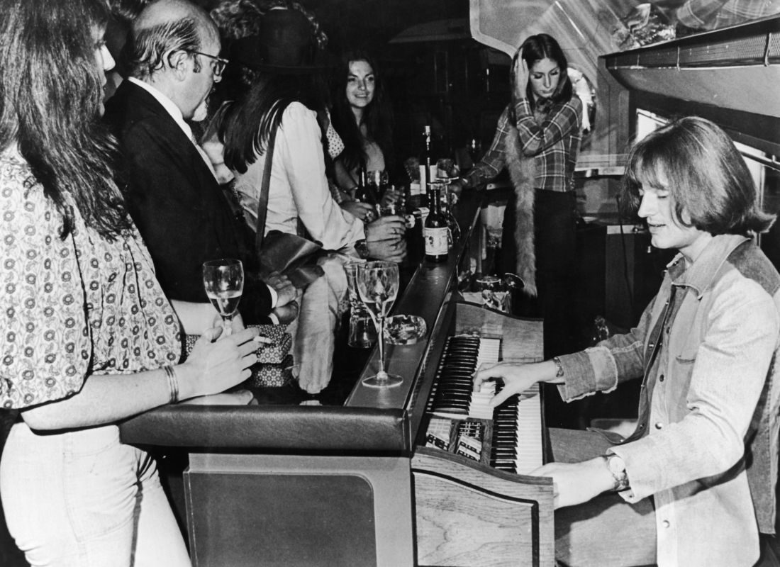 John Paul Jones of Led Zeppelin plays an electric organ behind the bar on board a private Boeing 720B airliner known as 'The Starship', which is being used by the band on their North American tour, 30 July 1973