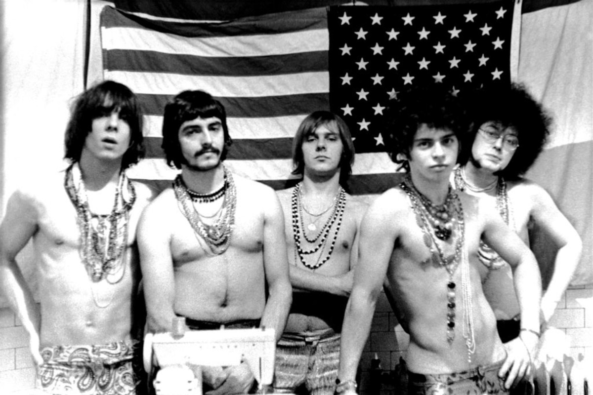 MC5 (L-R Fred "Sonic" Smith, Dennis "Machine Gun" Thompson, Rob Tyner, Wayne Kramer and Michael Davis) pose for a photo in front of an American flag in 1967