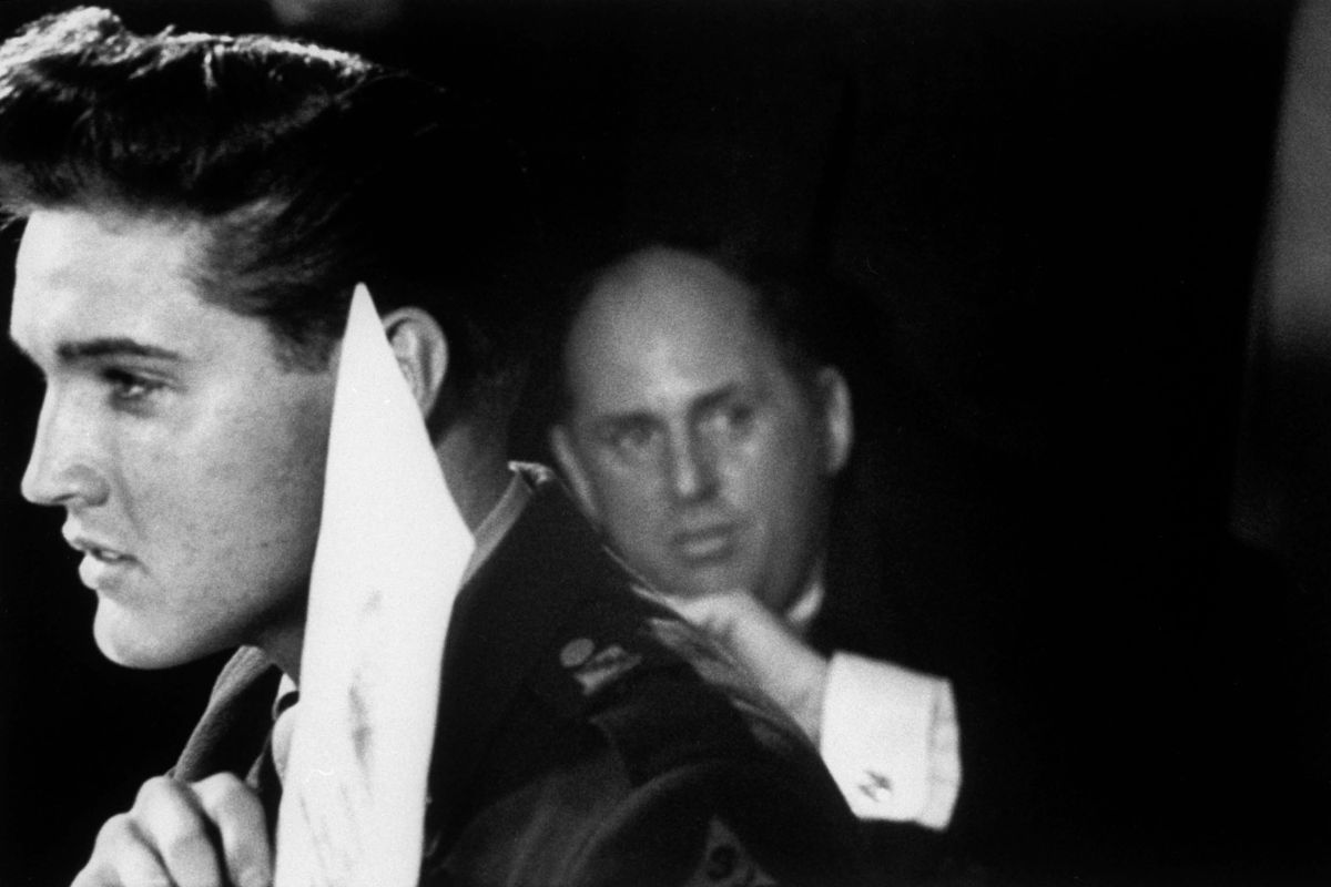 Elvis Presley holding up his US Army discharge paper, with his manager Colonel Tom Parker in the background