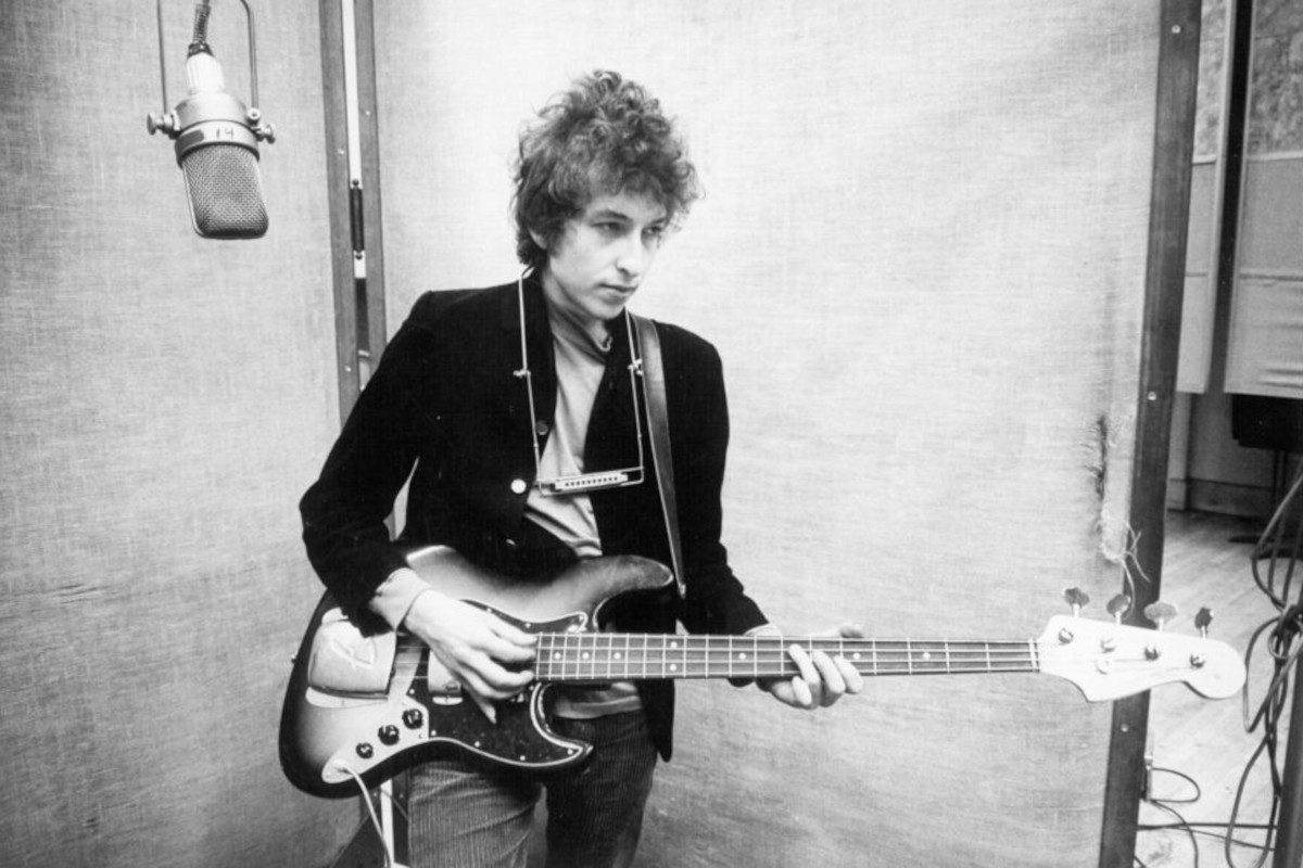 Bob Dylan plays a Fender Jazz bass with a harmonica around his neck while recording his album 'Bringing It All Back Home', circa January 1965