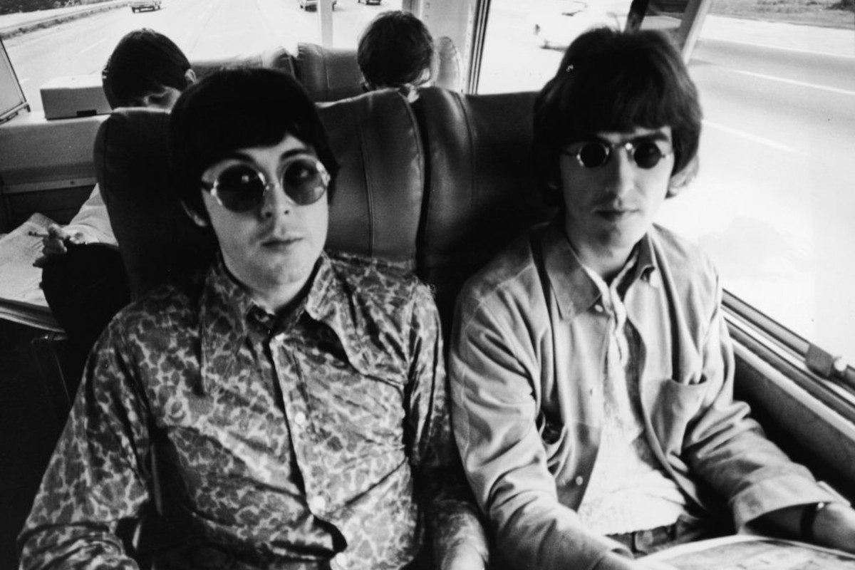 Paul McCartney and George Harrison sit next to each other on their tour bus during a Beatles American tour, c. 1966