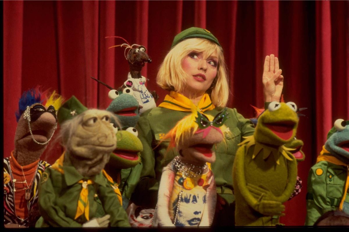 Blondie vocalist Debbie Harry giving a three-finger salute while dressed in a girl scout uniform on the set of The Muppet Show at Elstree Studios, Hertfordshire, circa August 1980